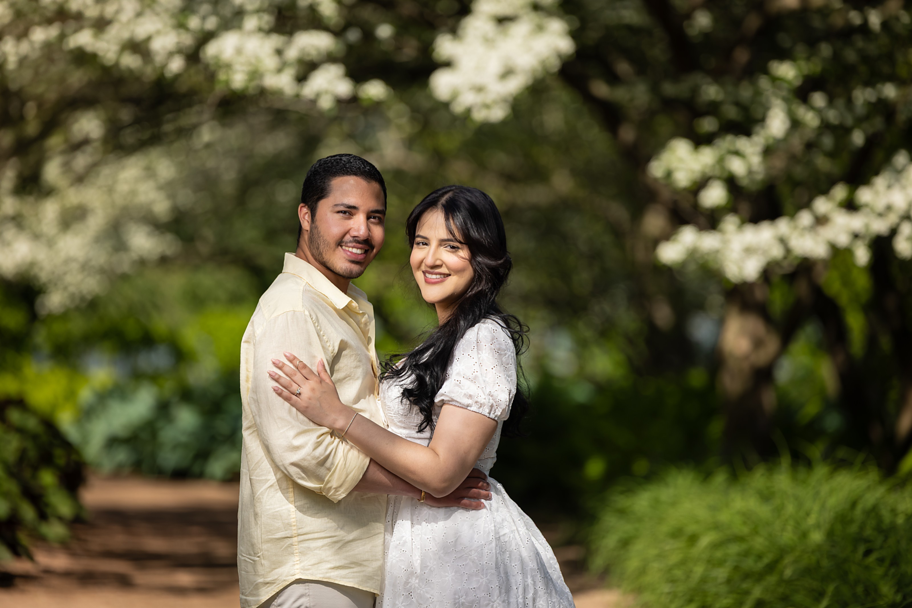 The newly engaged couple embracing and smiling beneath white flowering trees at the Chicago Botanic Garden