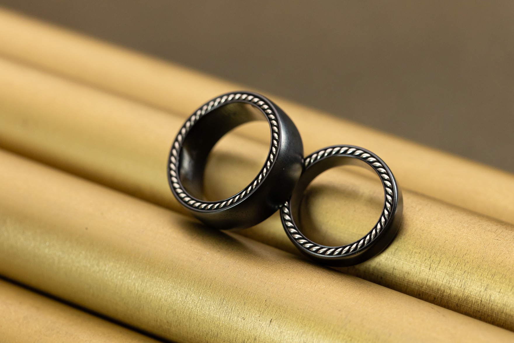 Two black wedding bands resting side by side on gold