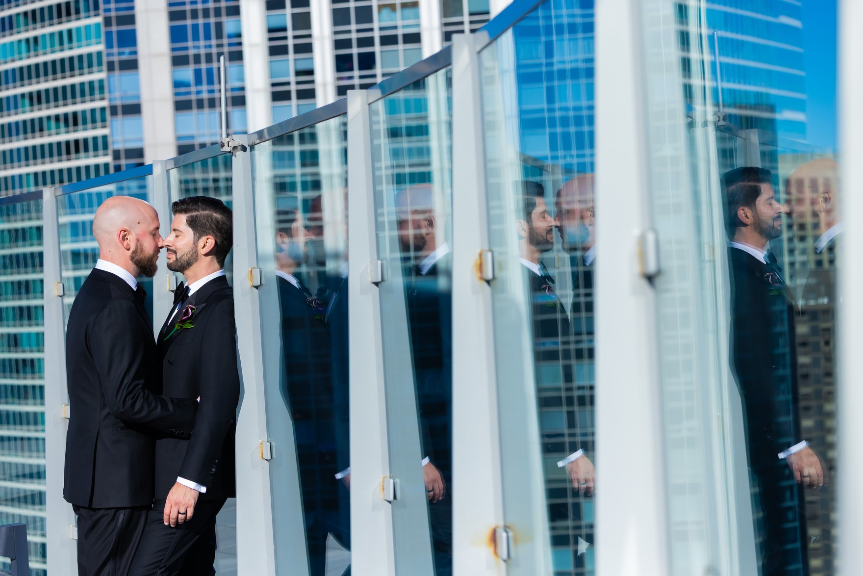The grooms touching noses, smiling, framed by glass panels