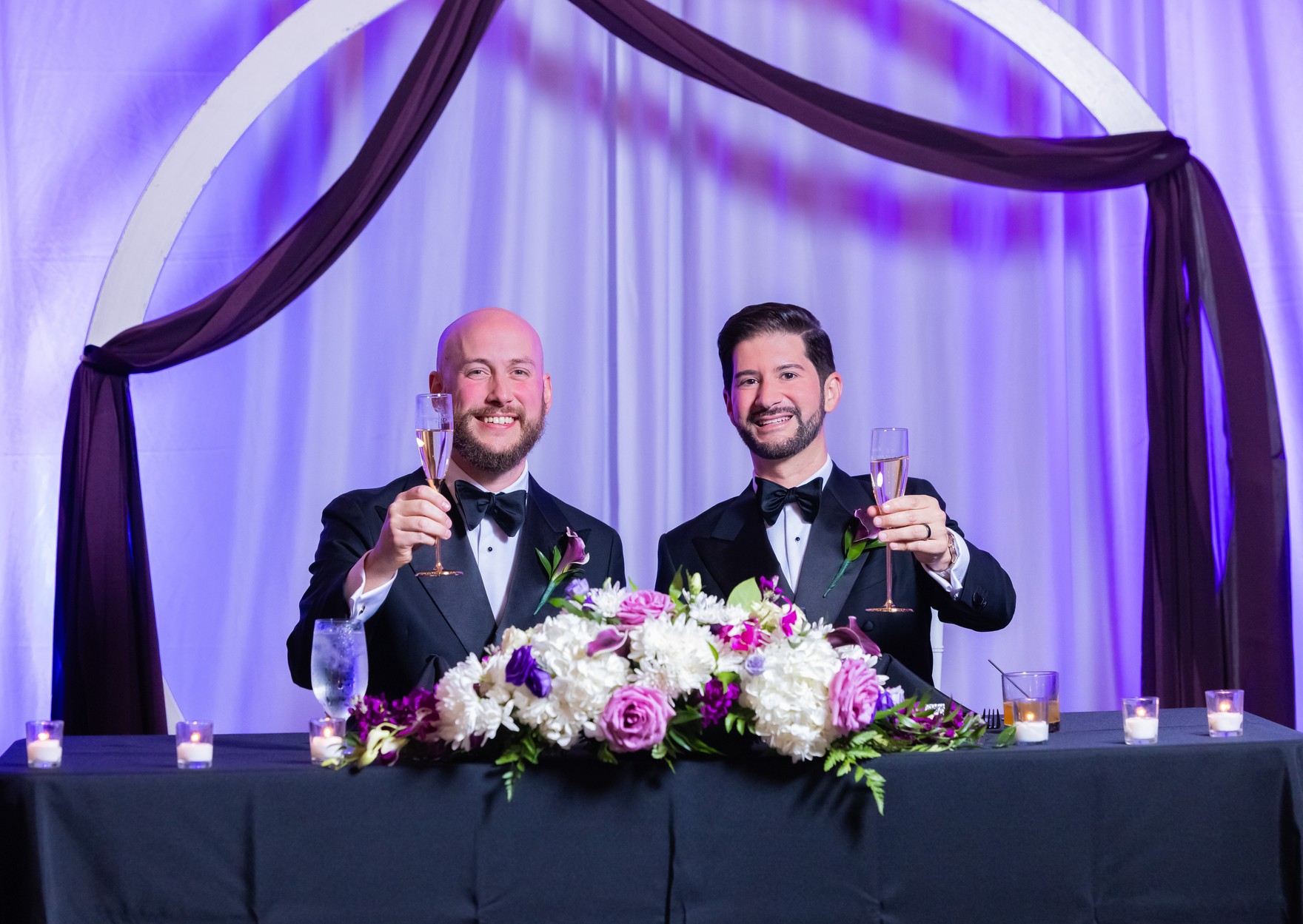 The grooms raising champagne glasses in a toast at their sweetheart table